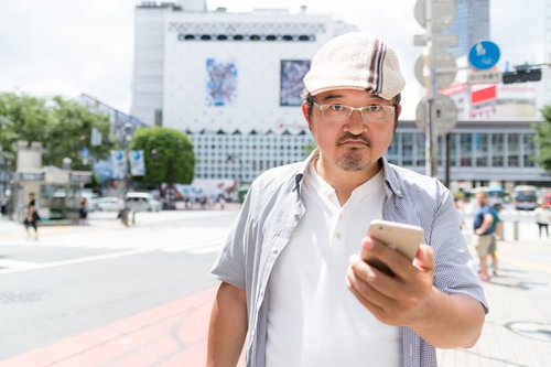 渋谷でスマートフォンを持つハンチング帽姿の男性