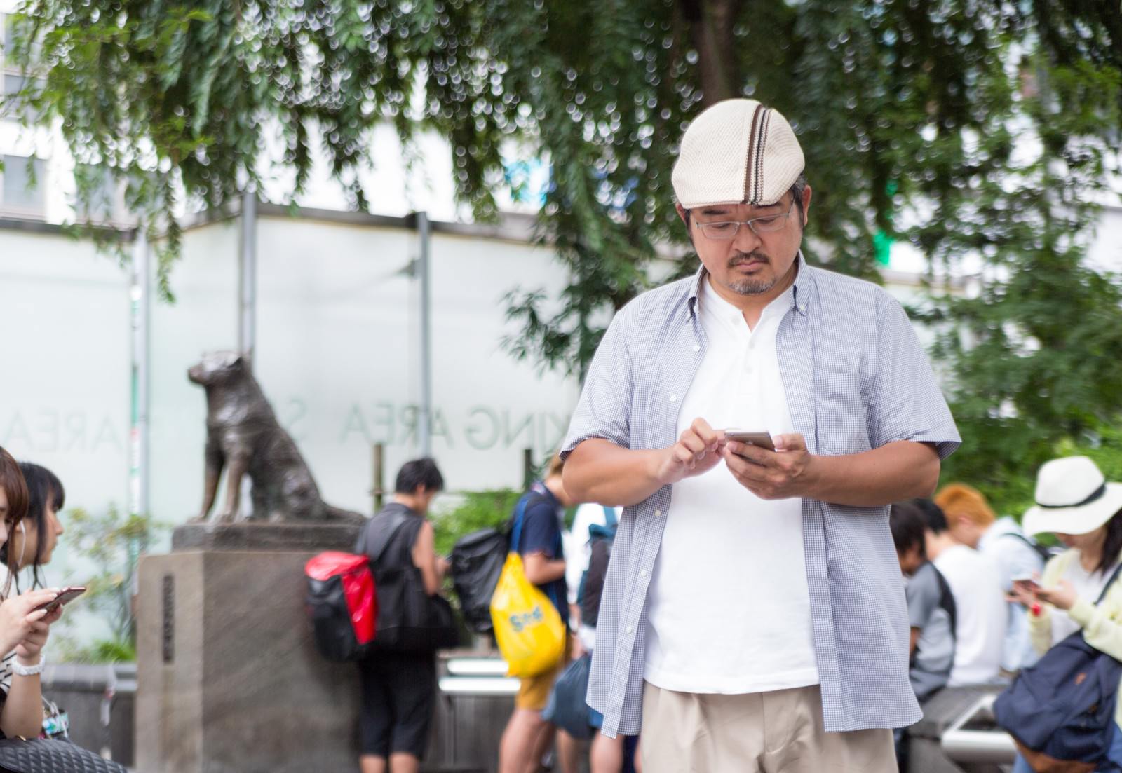 ハチ公像前でスマホを操作するハンチング帽の男性［モデル：ナリシゲ］