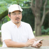 大人気のスマートフォン用ゲームに否定的な意見を述べるハンチング帽姿の男性の写真