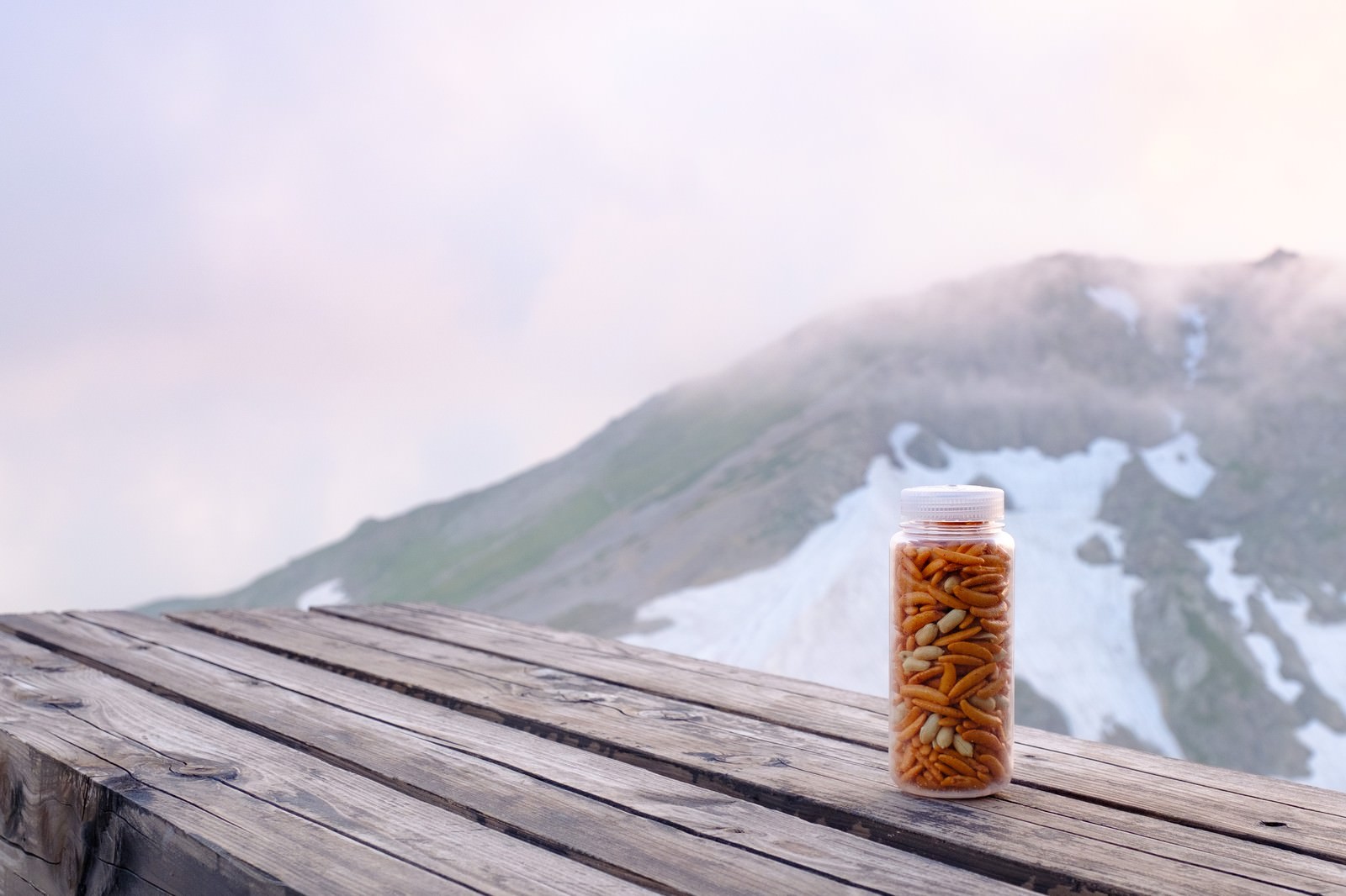 木製テーブルに置かれたナルゲンボトルに入った柿ピーと雪山の風景