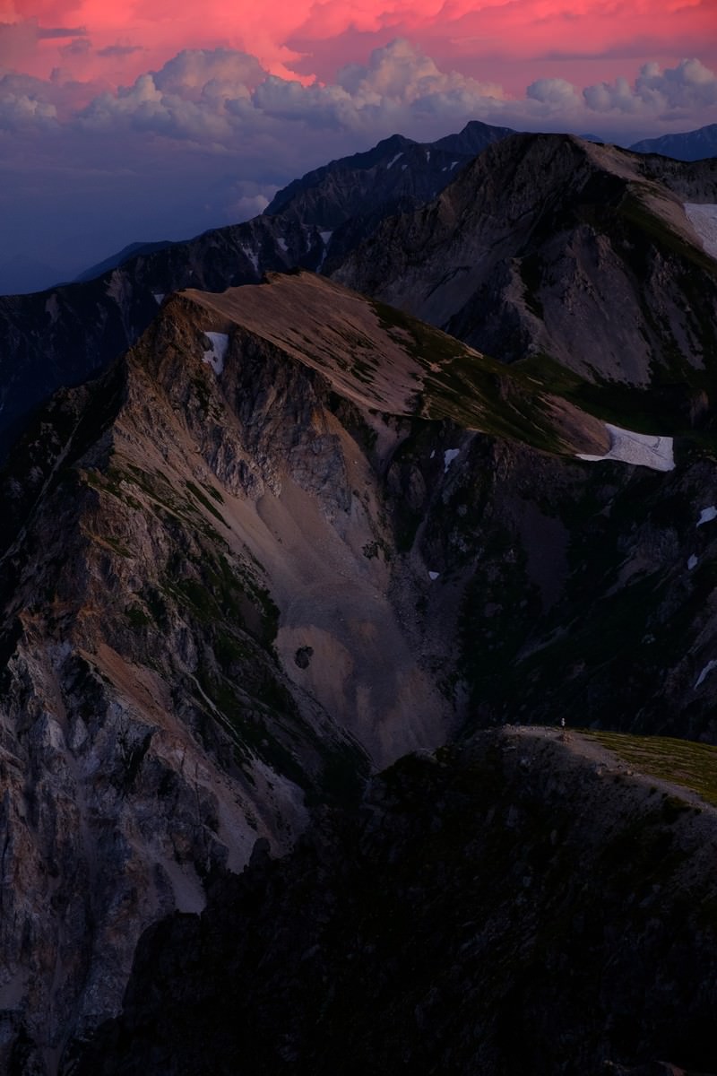 夕暮れ時にピンク色に染まった空を背景に、白馬連峰の山々のシルエットが連なる風景
