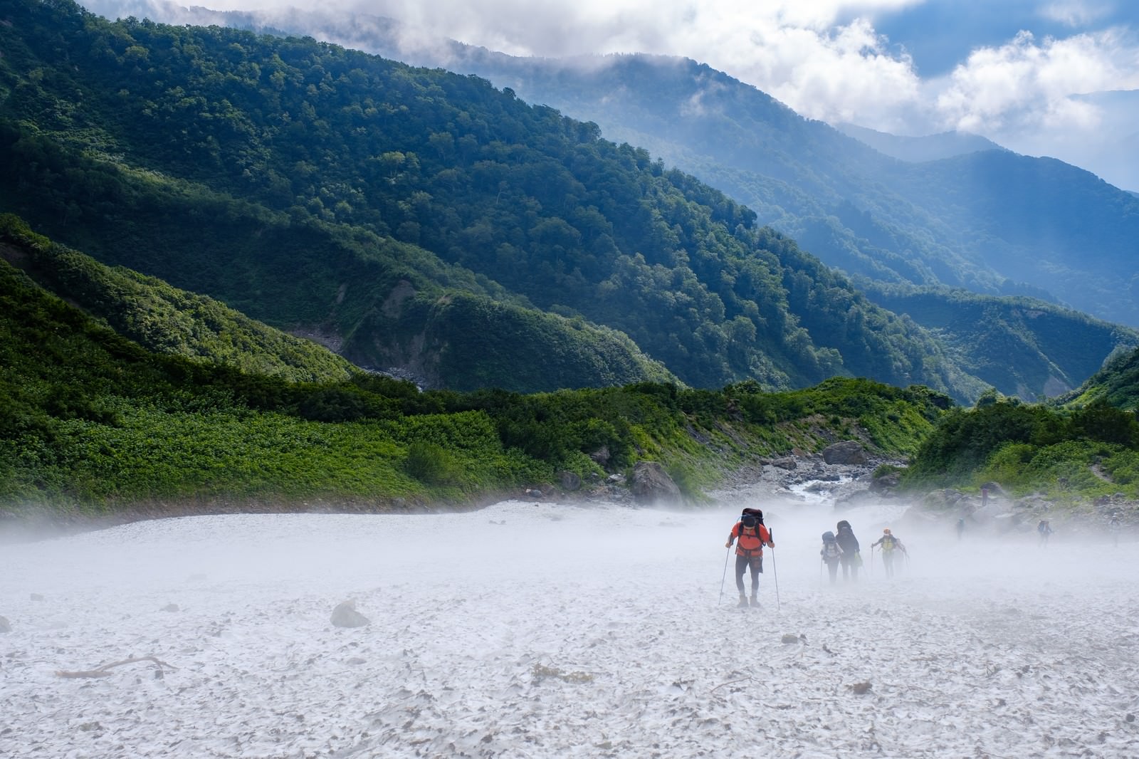白馬大雪渓の雪渓を登る複数の登山者達と背景の緑の山々