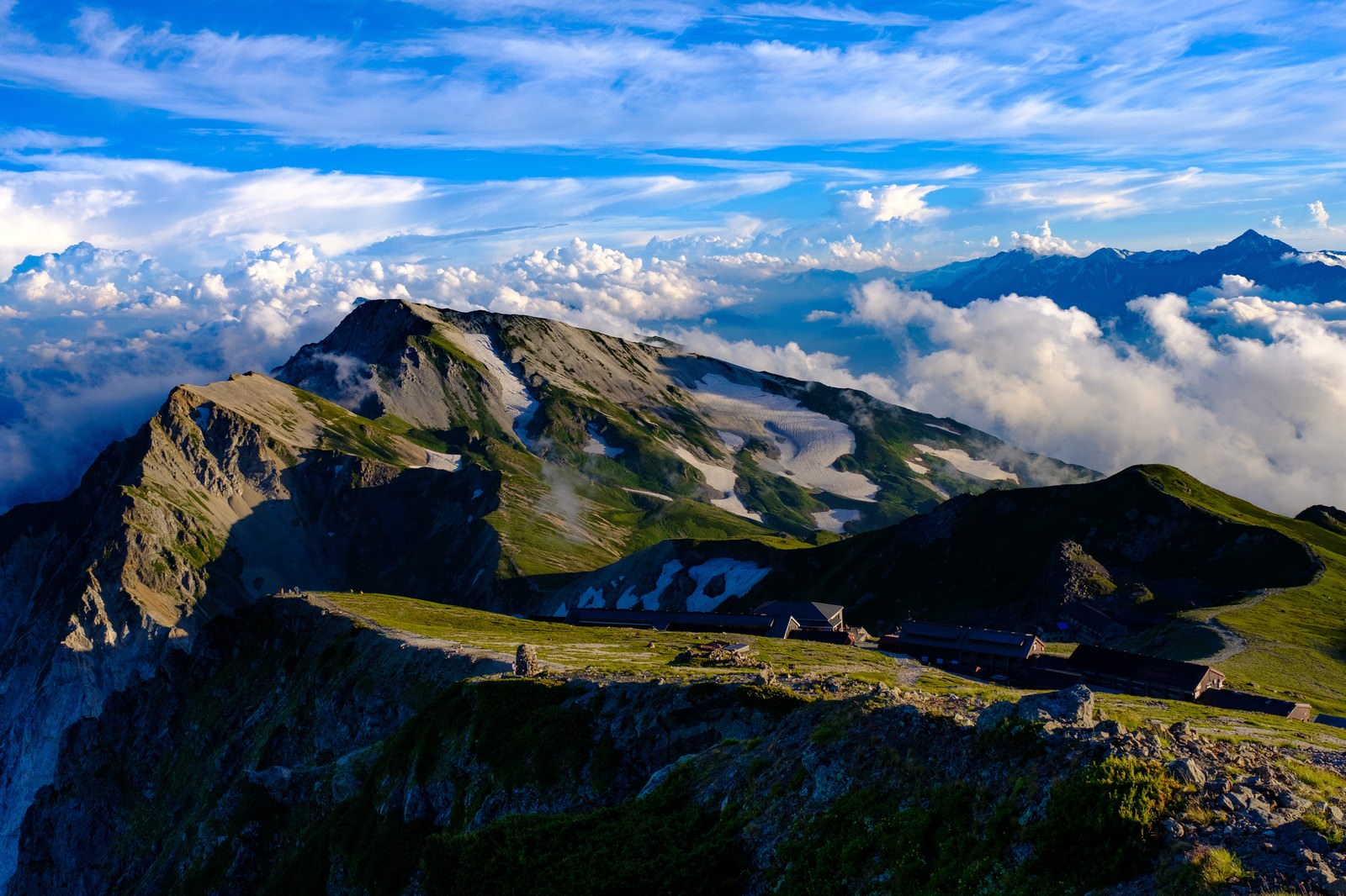 夕方の白馬連峰の雲海と緑の稜線、山荘が見える山岳風景