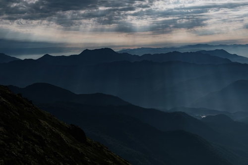 雲間から街へ降り注ぐ光芒と北アルプスの山々