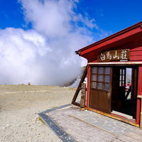 雲の隣に構える白馬山荘の山頂、登山者向けの山小屋の写真