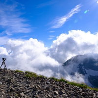 白馬岳山頂から眼下に見える雲と三脚を立てた登山者の写真
