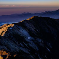 白馬岳山頂から望む夕日に染まる稜線と後立山連峰の写真
