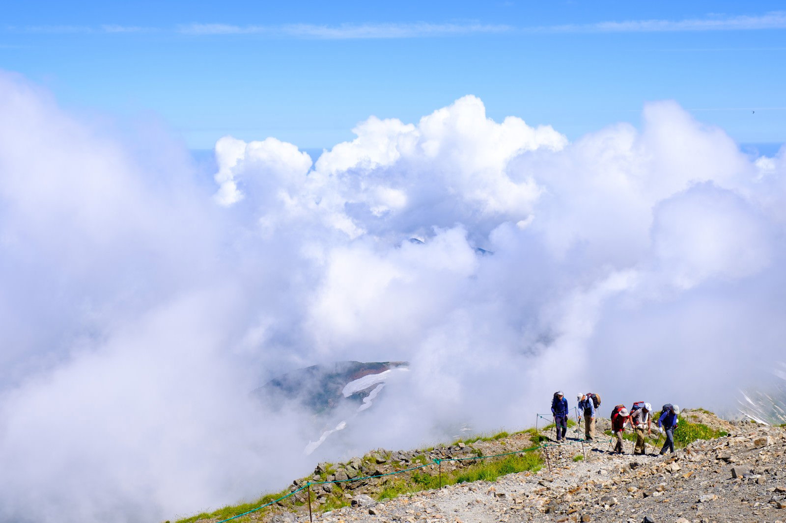 白馬岳の稜線を歩く登山者たちの後ろから白い雲が迫る山岳風景