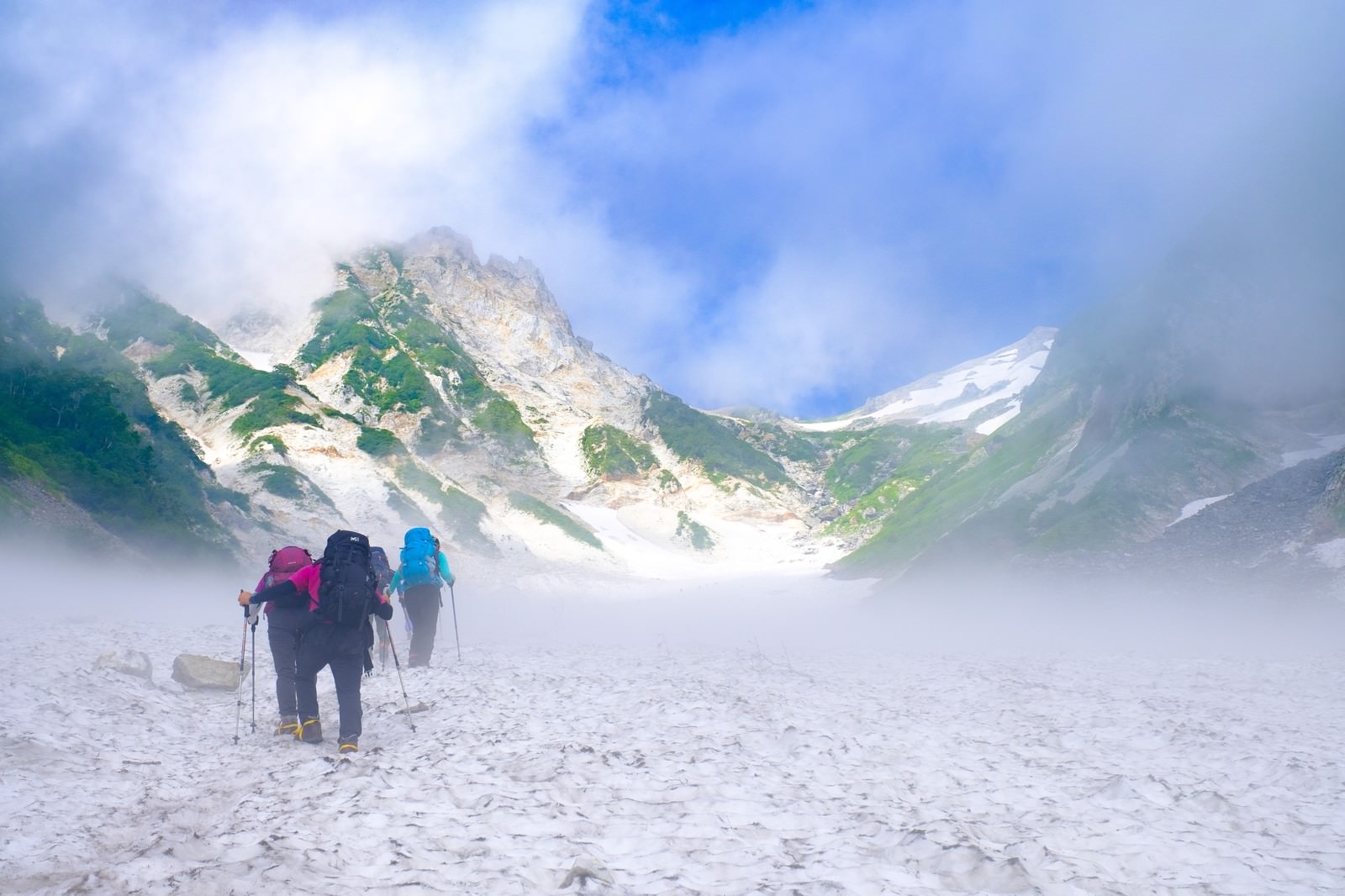 雪渓を一列になって登っていく3人の登山者の後ろ姿