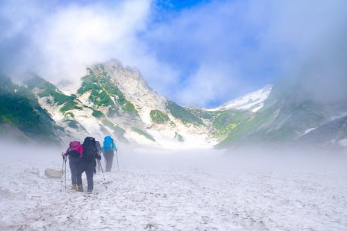 ガスの合間から見える白馬岳と白馬大雪渓を歩む登山者