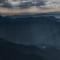 山間部の稜線から差し込む光と連なる山々の眺望の写真