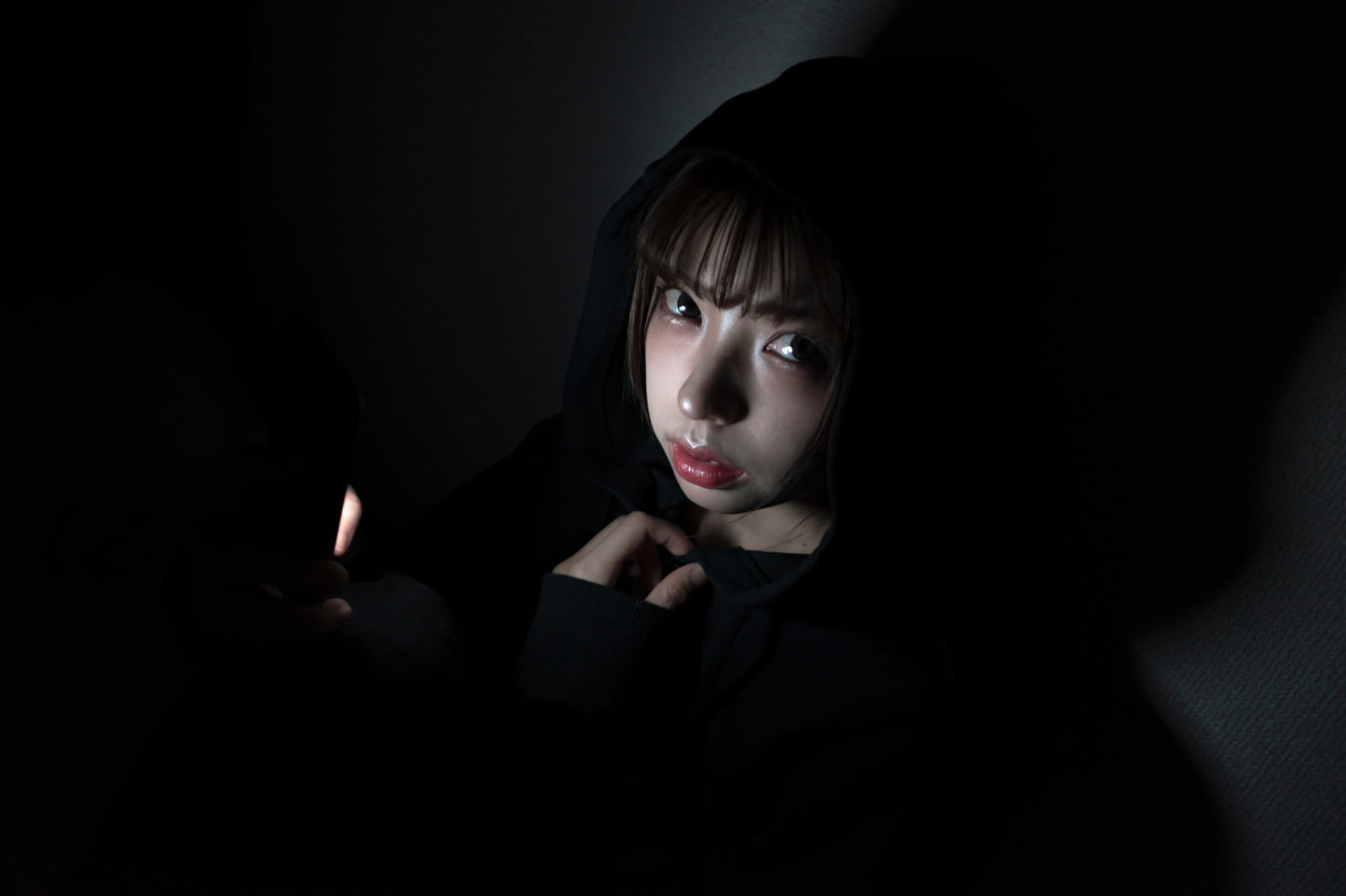暗い場所でスマートフォンの画面を見つめる女性の姿［モデル：高尾実生］