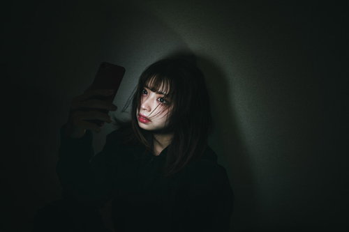 推しの裏垢を見つけた女性がスマートフォンを見つめている