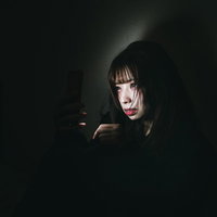暗がりでスマートフォンを見つめる廃課金女子の写真