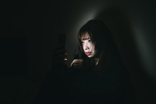 暗がりでスマートフォンを見つめる廃課金女子