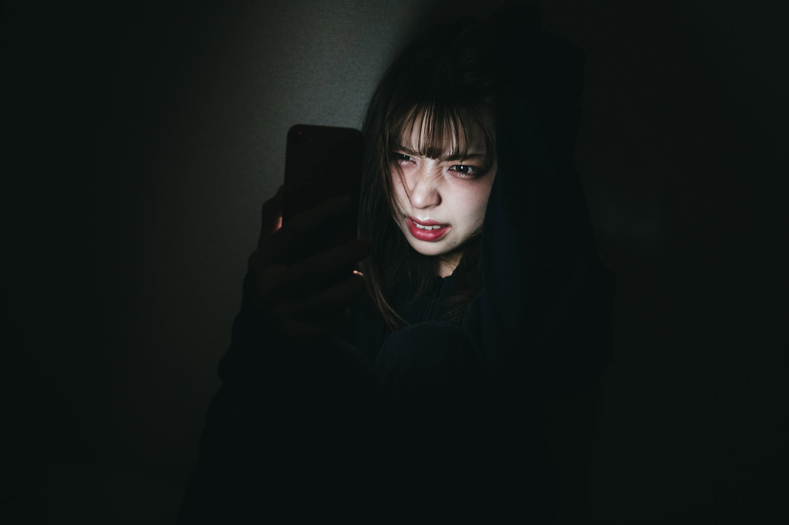 暗い背景でスマートフォンを手に持つ女性［モデル：高尾実生］