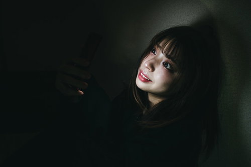 他人の不幸は蜜の味ィィ　暗がりでスマートフォンを見つめる女性