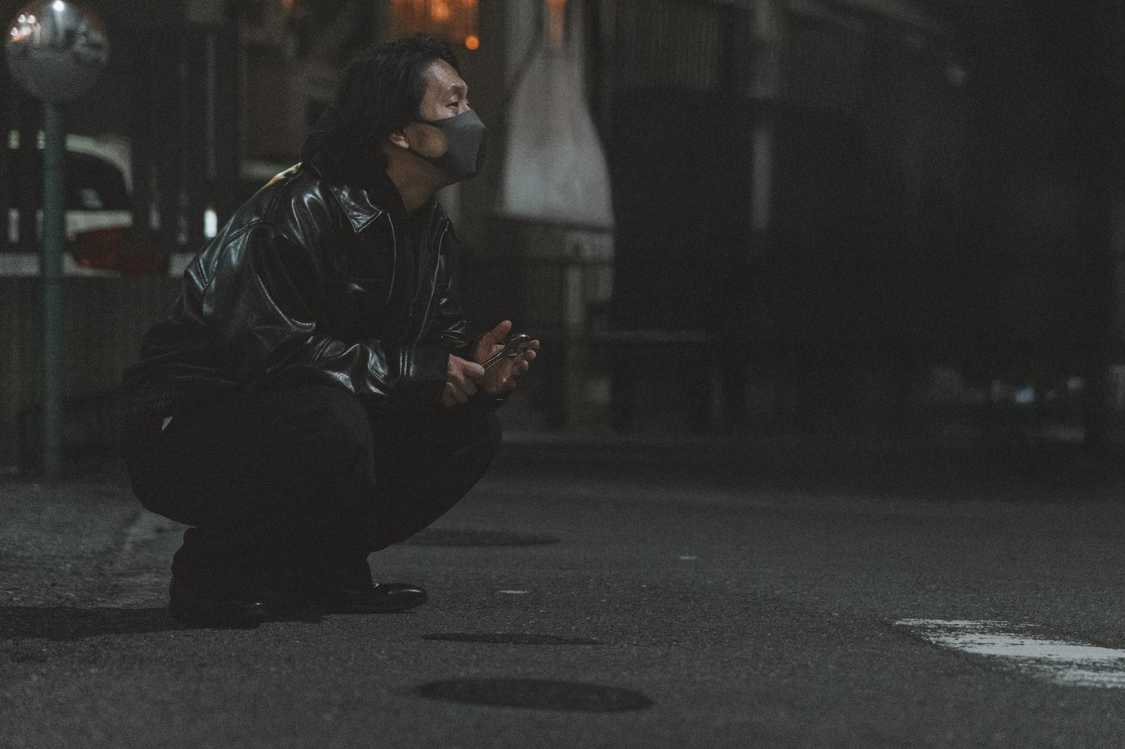 深夜に懐中電灯を持ってしゃがむ黒い服の男性［モデル：大川竜弥］
