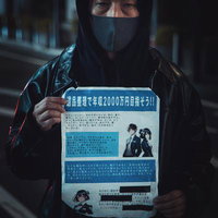 黒フード姿で怪文書を掲げる男性の夜間路上シーンの写真