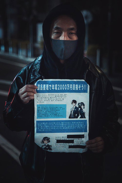 黒フード姿で怪文書を掲げる男性の夜間路上シーン