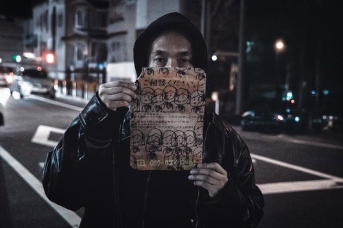 夜の街角で怪文書を持つフード姿の男性
