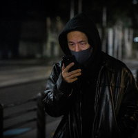 黒ずくめでマスク姿、夜間の路上にいる男性の写真