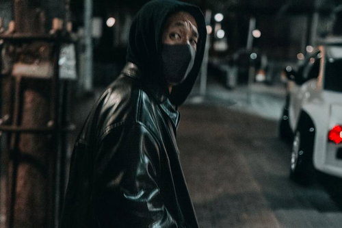 夜間の路上でフードを被った不審な男性の後ろ姿