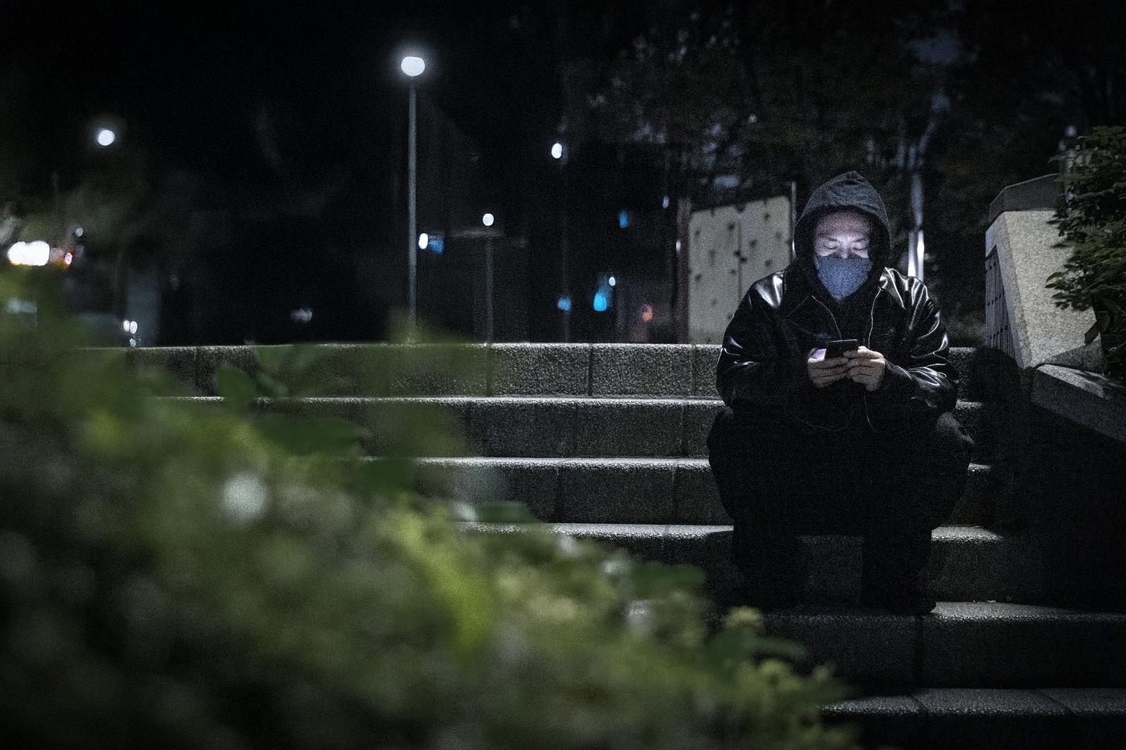 夜間の階段でスマートフォンを見ながら指示を待つ黒ずくめの男性［モデル：大川竜弥］
