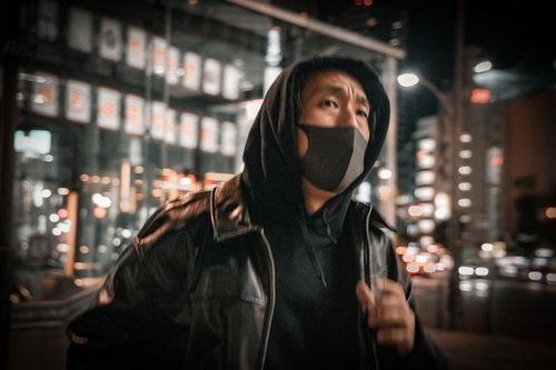 繁華街の夜間で走る黒いマスク姿の男性の逃走シーン