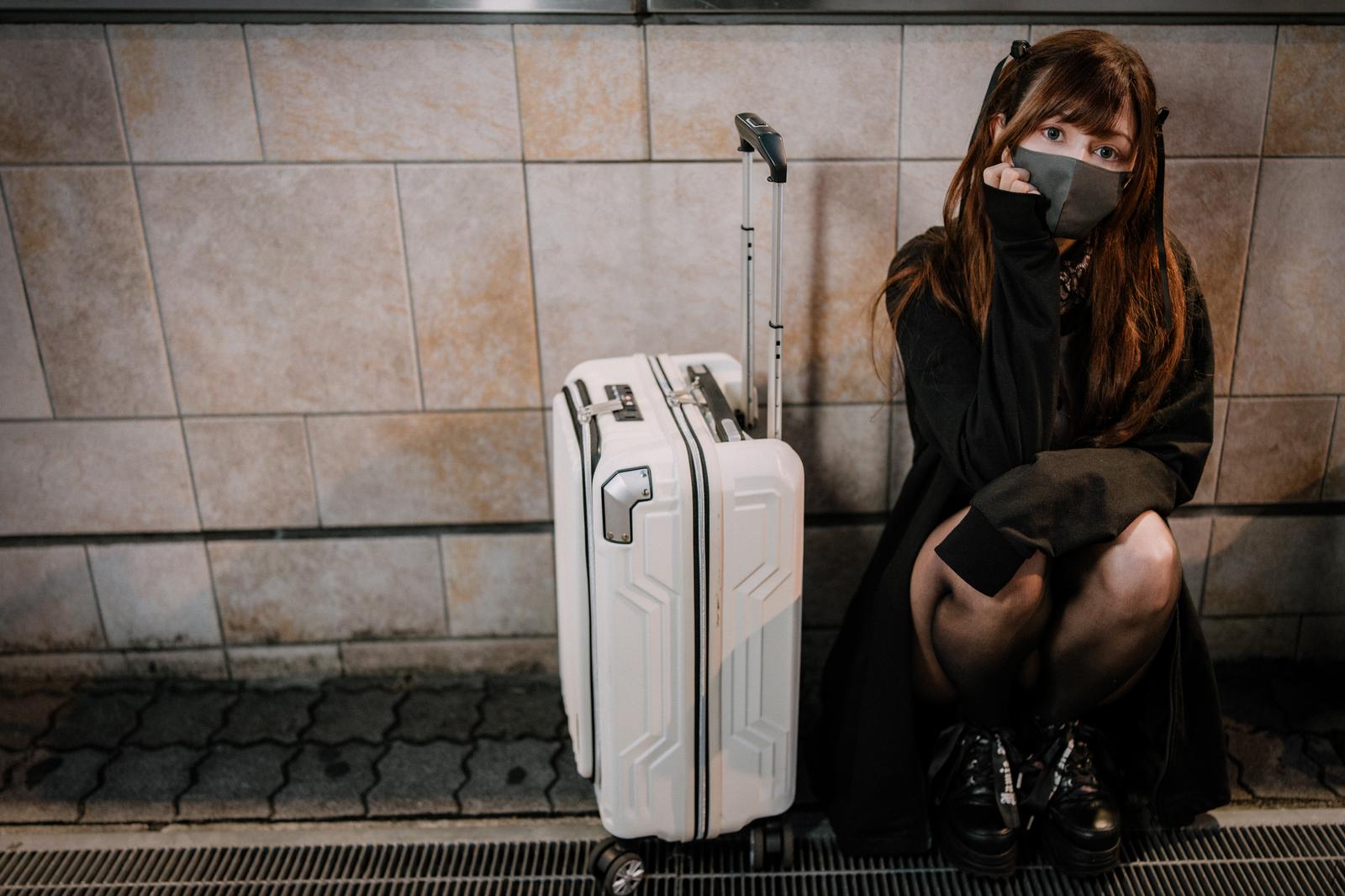 深夜に駅構内でキャリーケースの隣に座り込む女性［モデル：ラミエル］