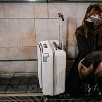 深夜に泊まるところがなくて駅前でキャリーケースを持って座り込むマスク女子の写真