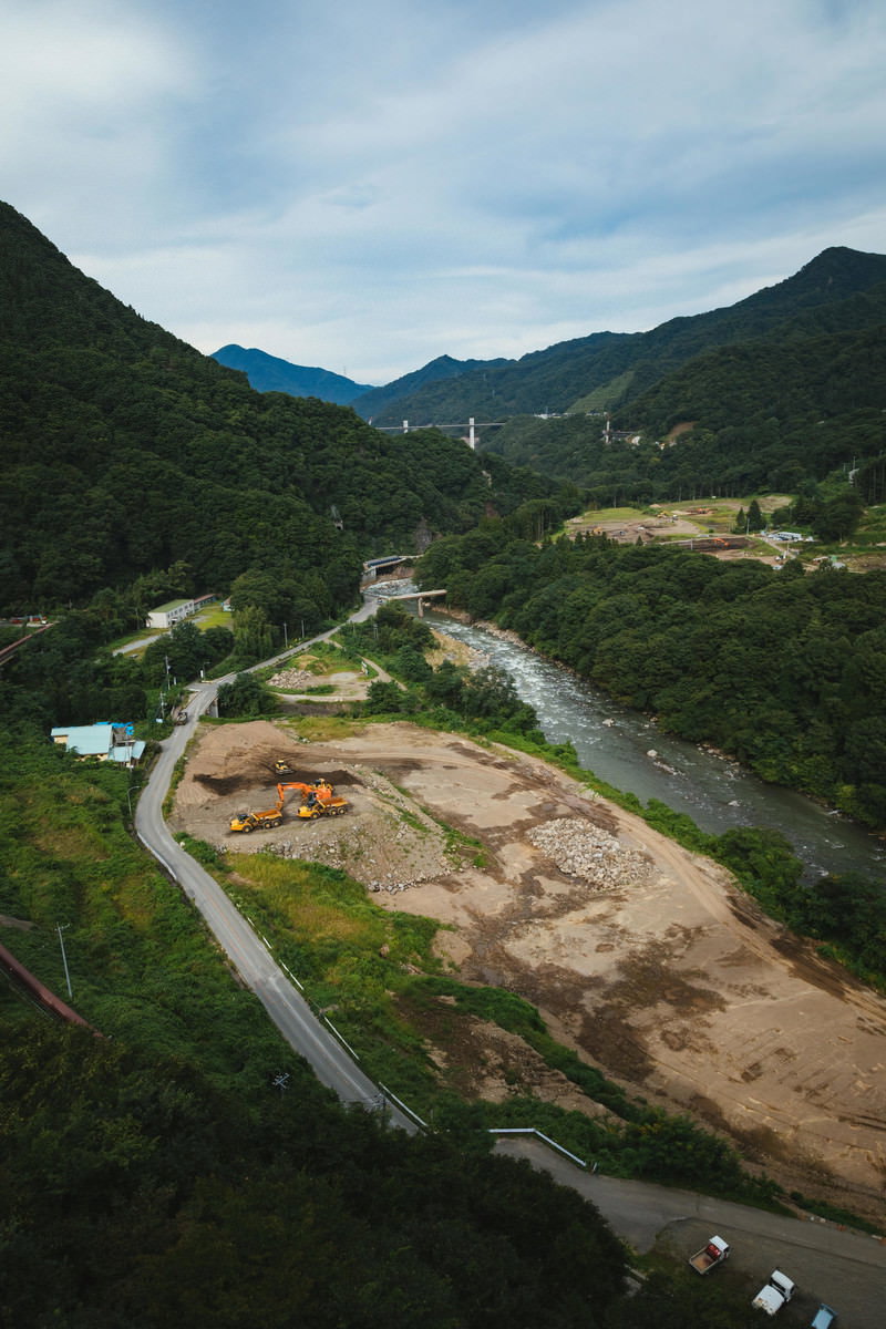 緑の山々に囲まれた川沿いで進行中の八ッ場ダム建設工事現場