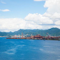 広島の海峡越しに見える工場と緑の山々、青空の風景の写真