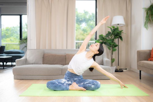 緑色ヨガマットの上でサイドストレッチポーズをとる白いウェアの女性