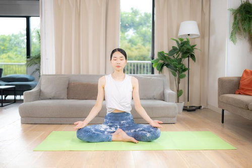 緑のヨガマットで蓮華座瞑想する白いタンクトップの女性