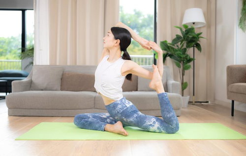 白いトップと青柄レギンスでエーカパーダラージャカポタアーサナを行う女性