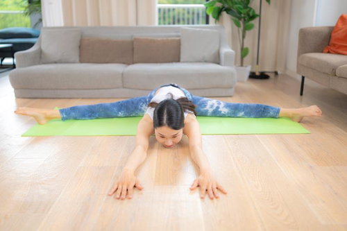 緑ヨガマットで開脚前屈ストレッチをする女性