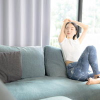 グレーソファで両手を上げてストレッチする白Tシャツの女性の写真