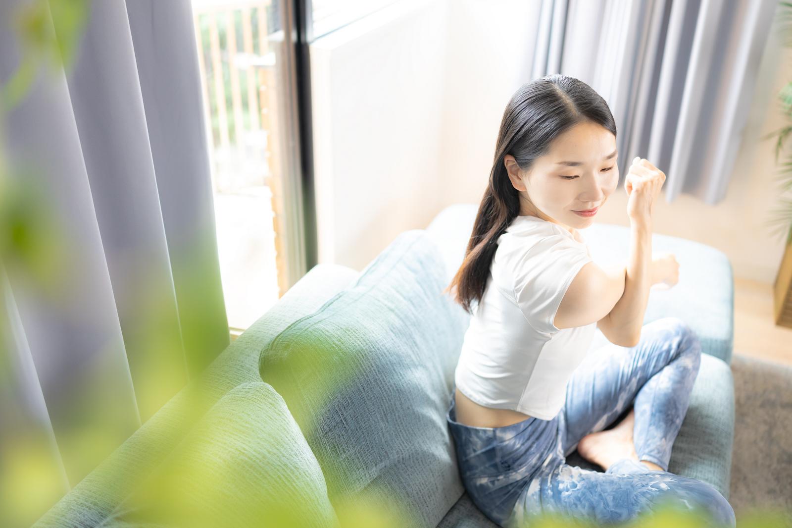 白いソファの上で目を閉じてストレッチをする女性［モデル：ひるかわえみこ］