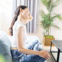 白いソファでストレッチする女性と観葉植物のあるリビングの写真