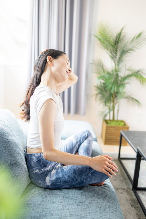 白いソファでストレッチする女性と観葉植物のあるリビング