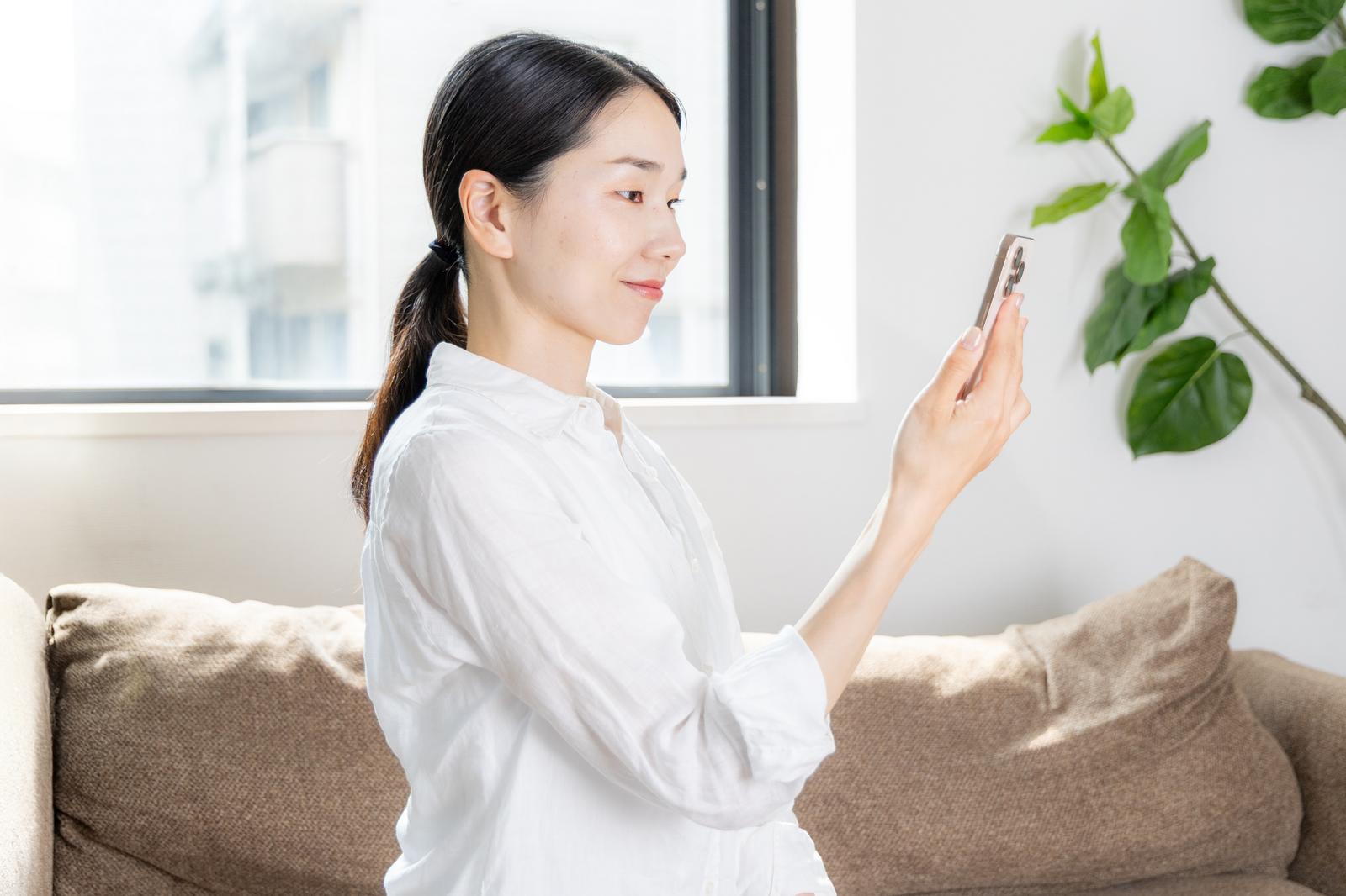 白いシャツの女性がソファでスマートフォンを正しい姿勢で操作［モデル：ひるかわえみこ］