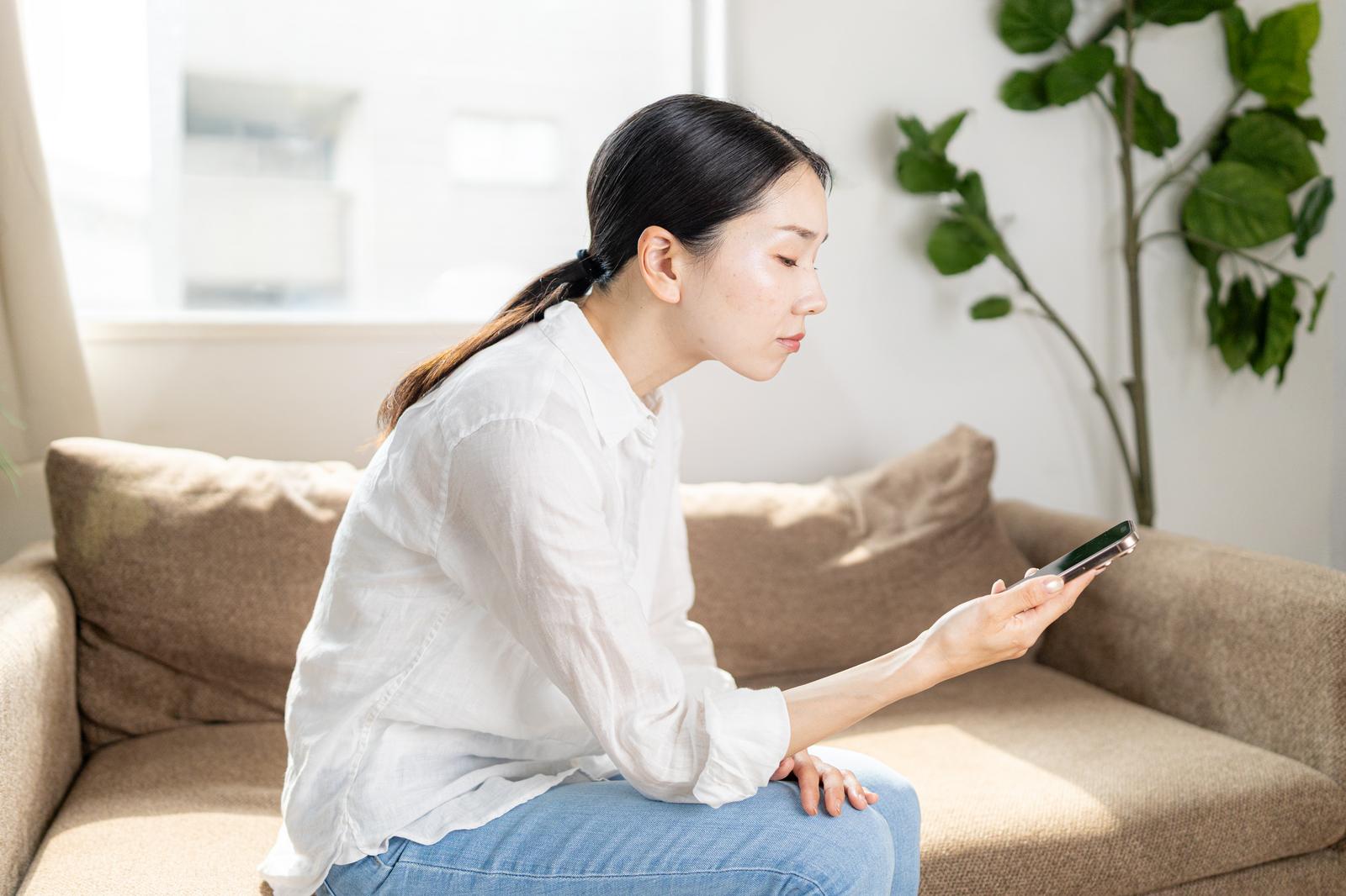 ソファでスマートフォンを見る女性［モデル：ひるかわえみこ］