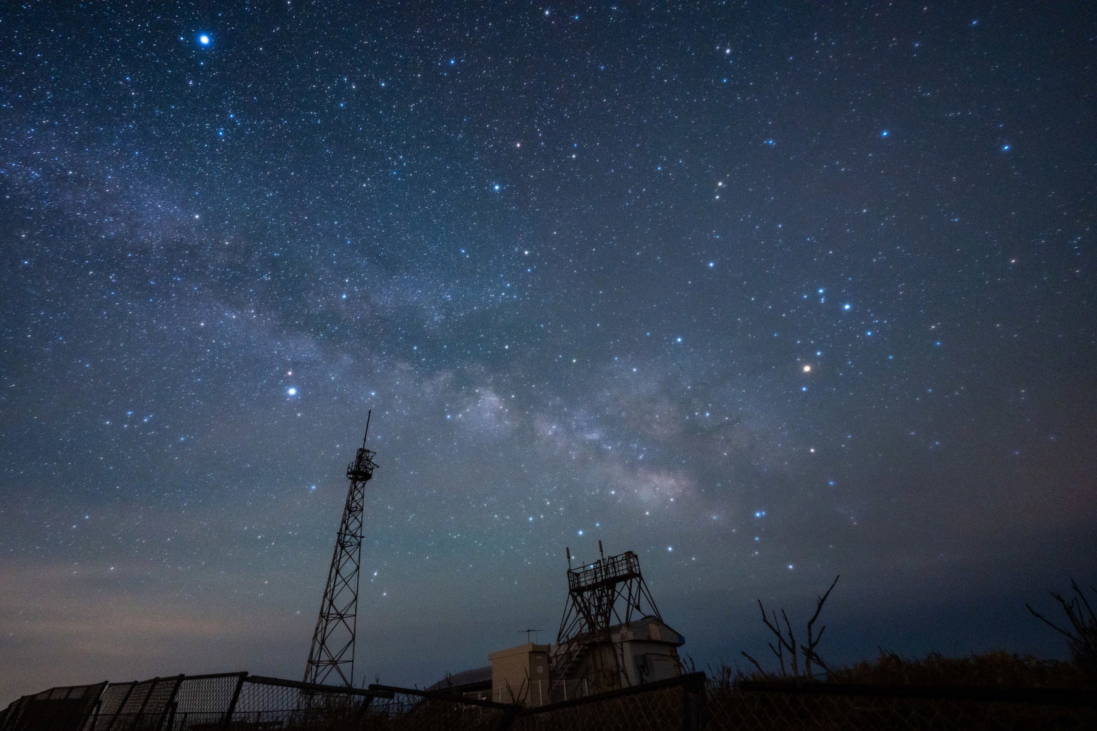 夜空に浮かぶ天の川を背景に、鉄塔のシルエットが映る星空の風景