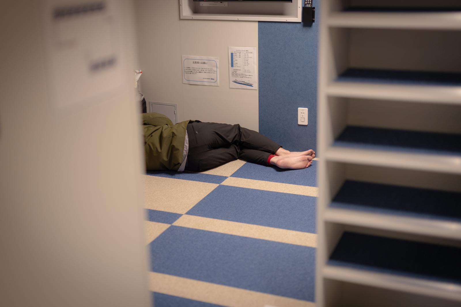 フェリーの畳敷き和室で仰向けに横になっている人