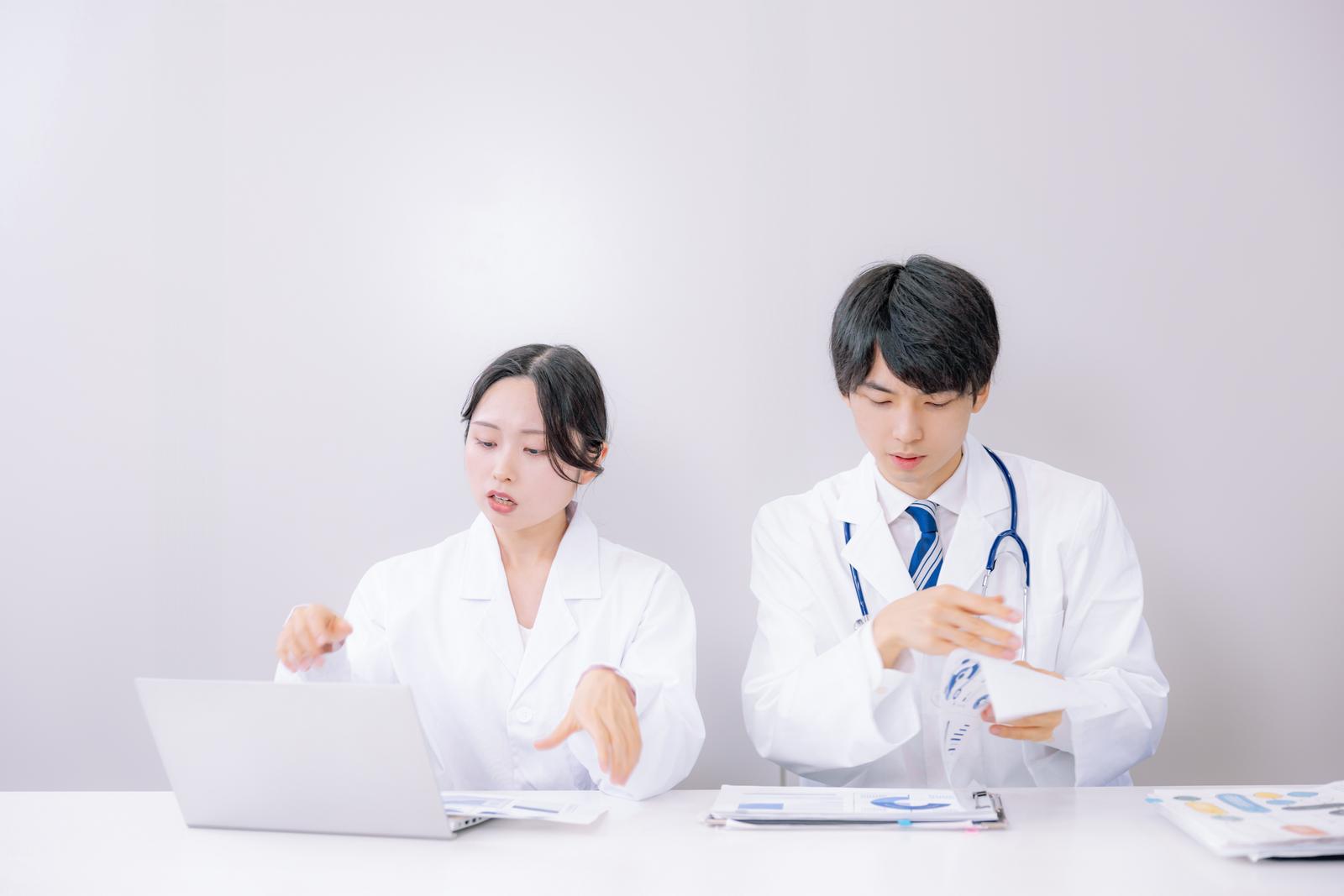 デスクで診療記録を確認する白衣の医師たち［モデル：たくみ 吉屋ゆり］