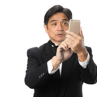 スマートフォンの操作に慣れない黒いスーツの執事の写真