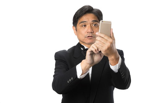 スマートフォンの操作に慣れない黒いスーツの執事