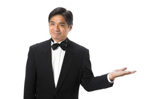黒いタキシードで笑顔で案内する支配人、蝶ネクタイ着用