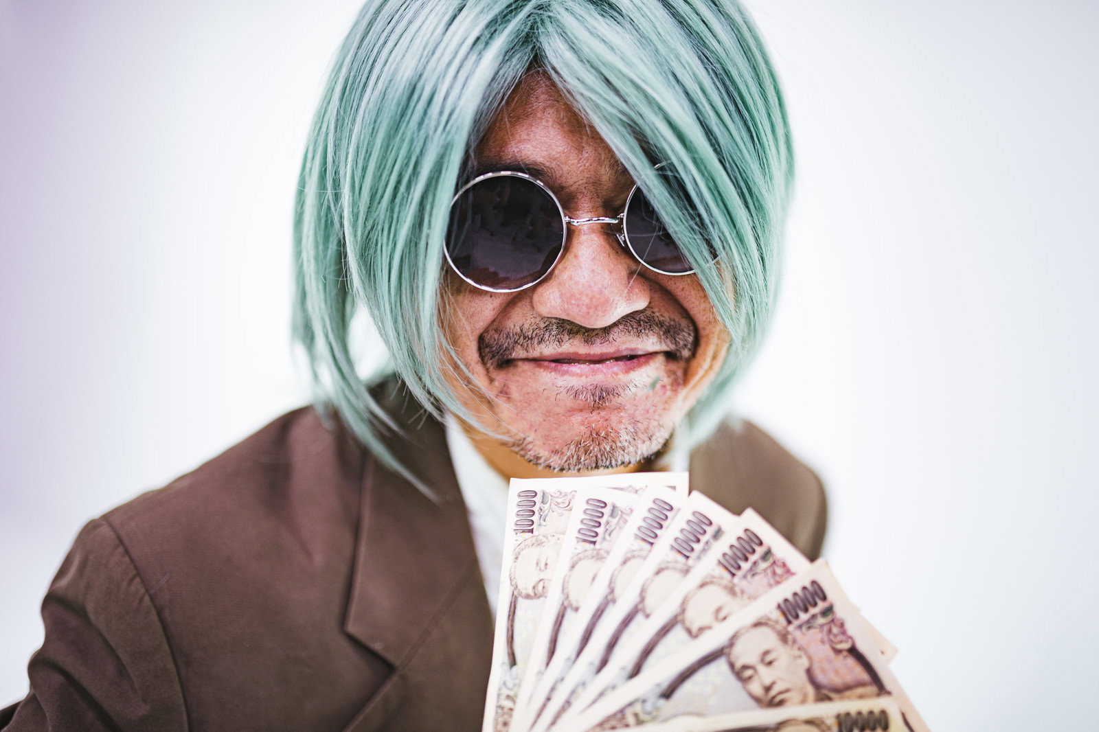 サングラスをかけて緑のウィッグを被った男性が一万円札を持つ［モデル：よたか］